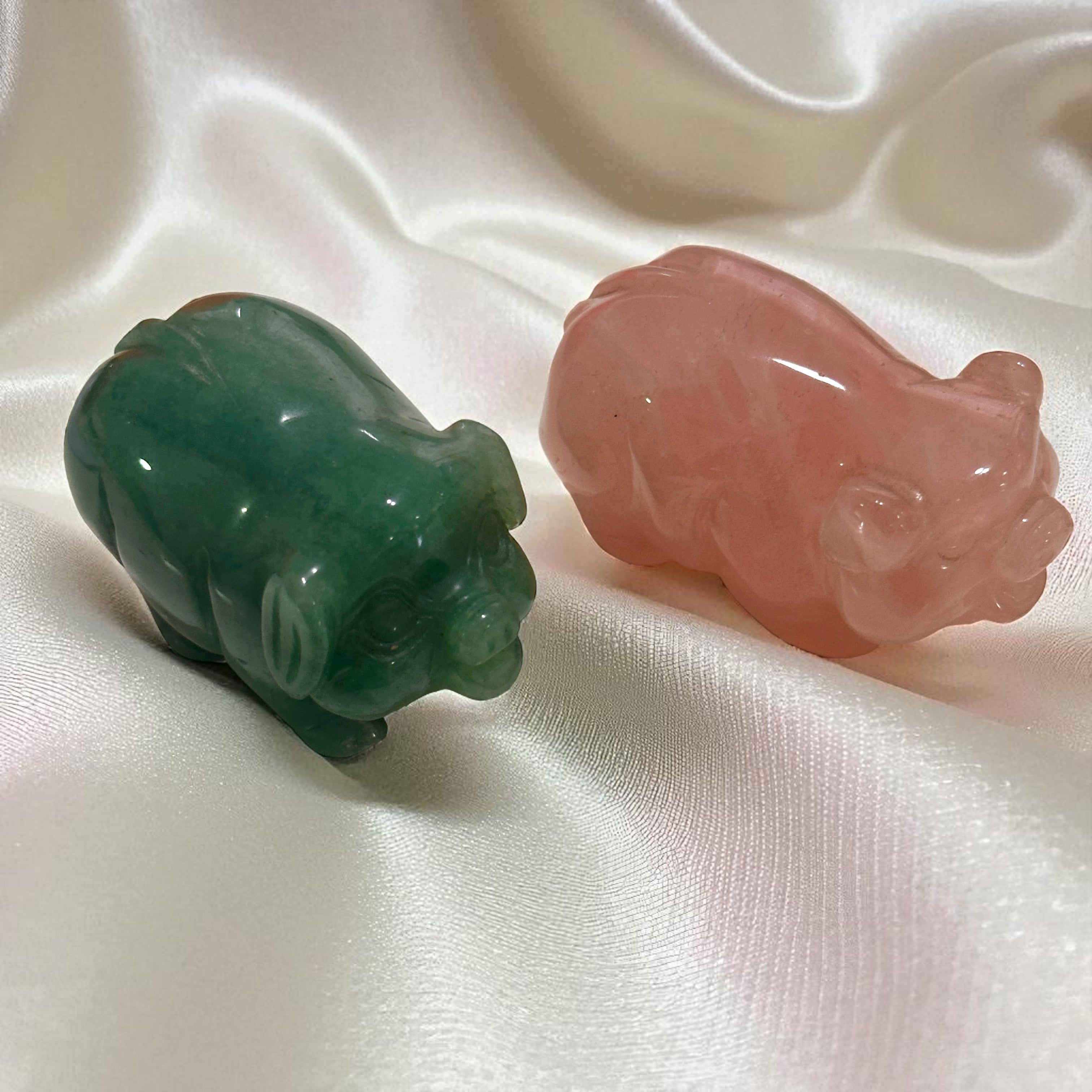 Two crystal pig figurines, one green and one pink, on a white fabric background.